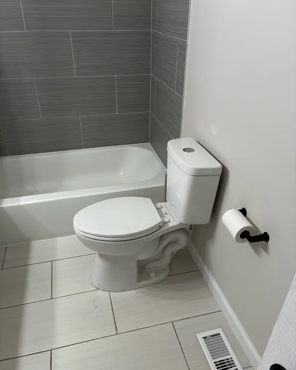 White bathtub and toilet with grey wall tile and a light tile floor