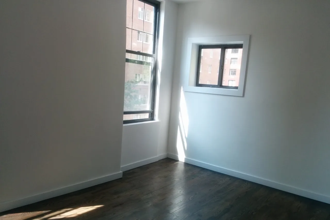 An empty apartment room with hardwood floors and two windows