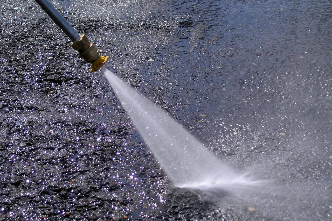A pressure washer nozzle spraying water across pavement